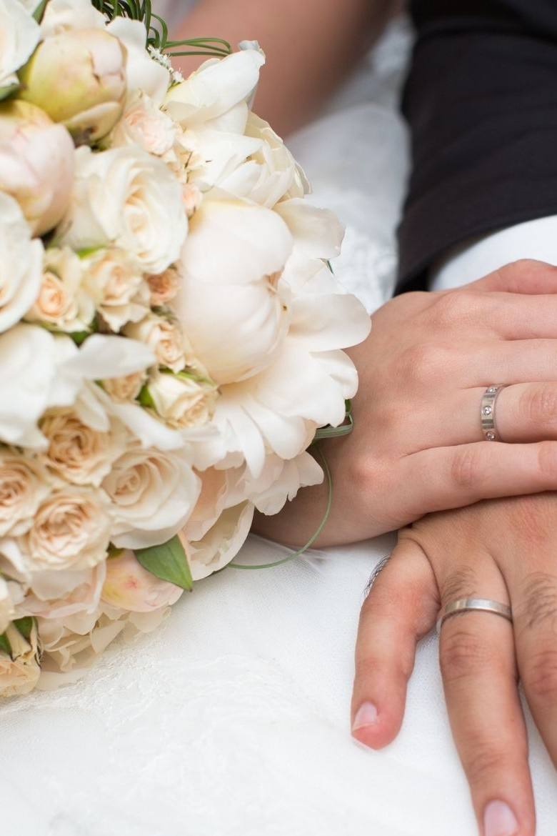 Les mains des mariés avec leurs alliances, sur le bouquet