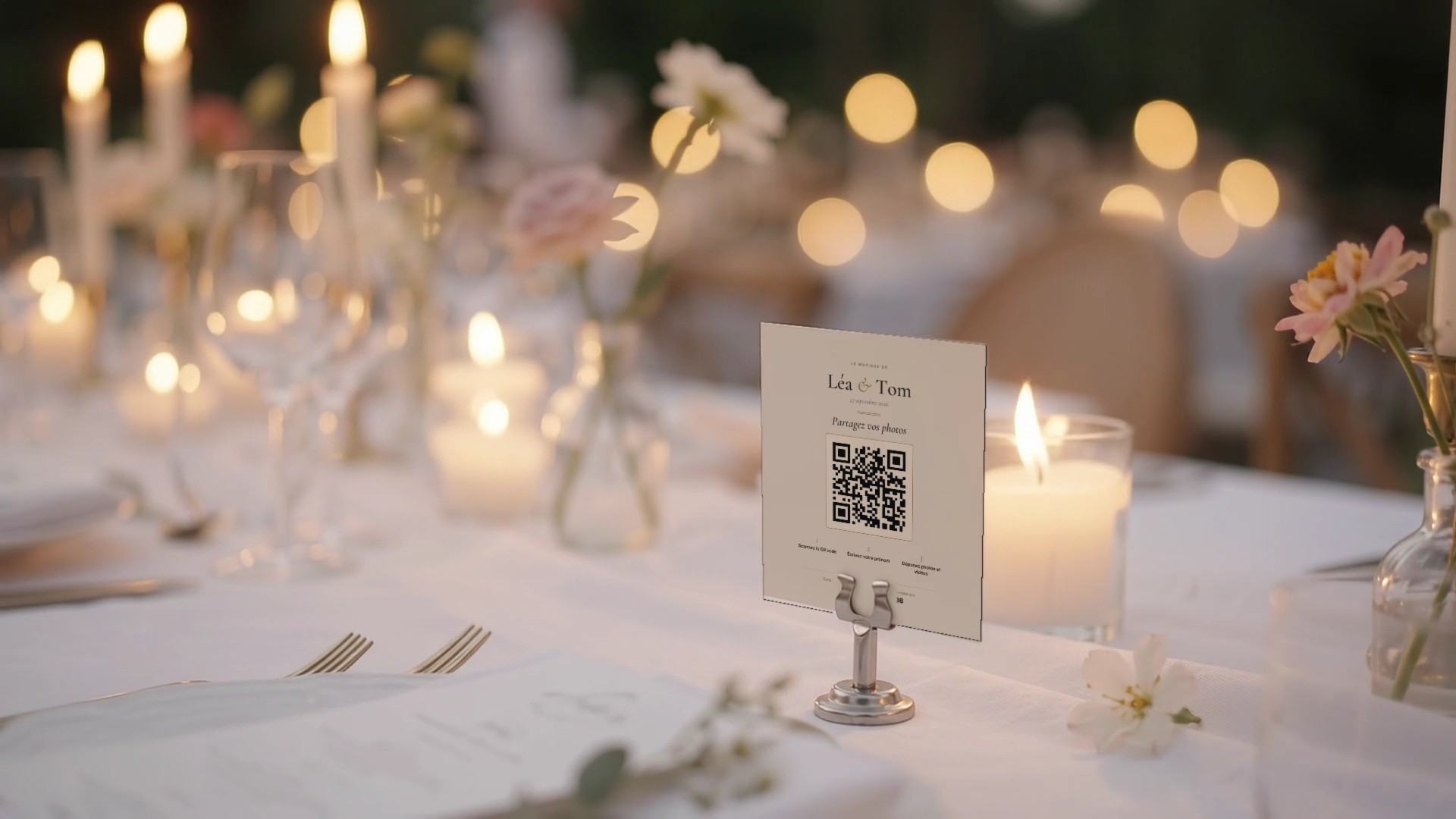 Une carte de table avec le QR code des mariés, posée sur la table du mariage à côté d’une bougie