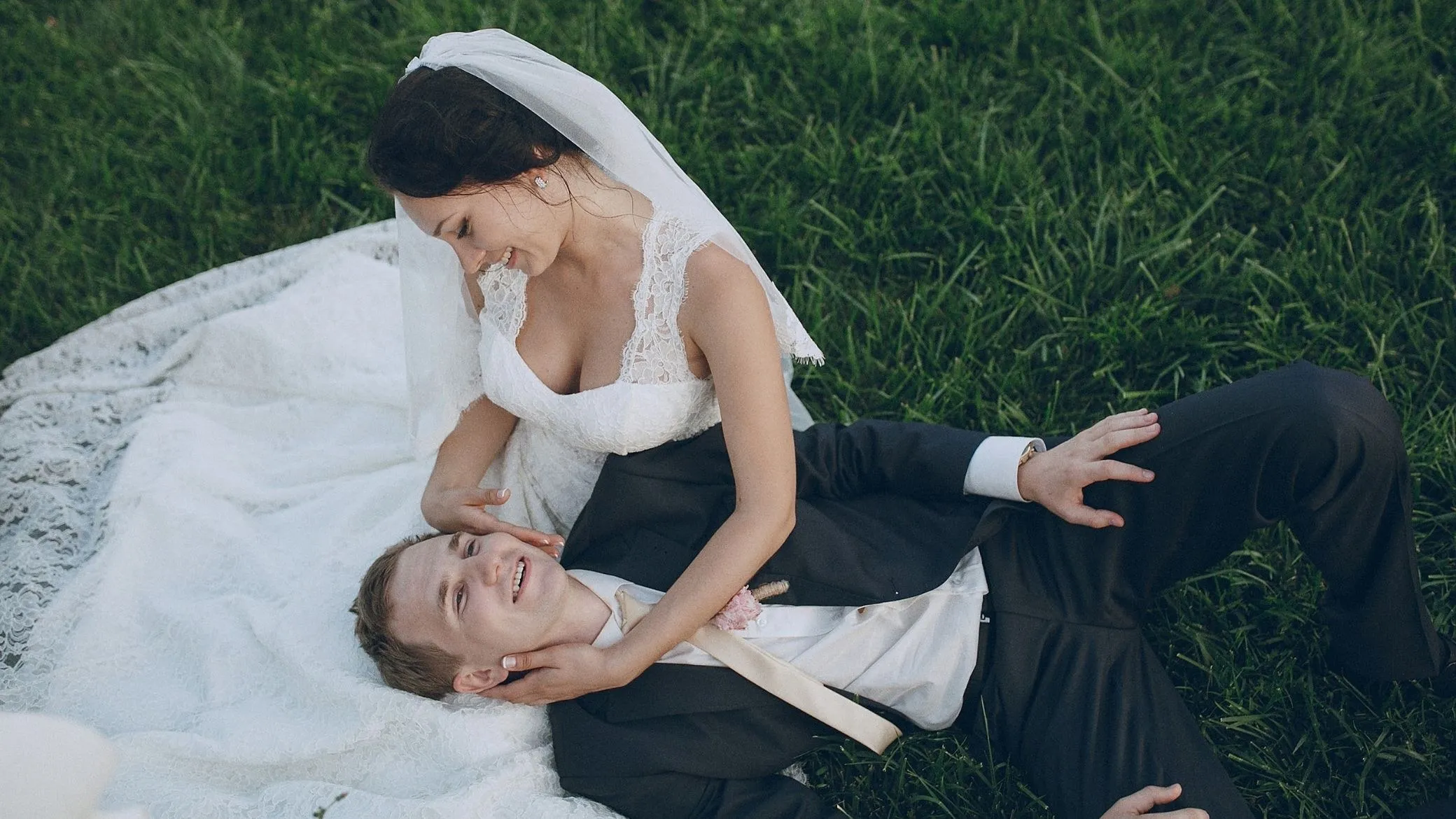Les mariés rient dans l’herbe : la mariée est allongée sur les genoux du marié