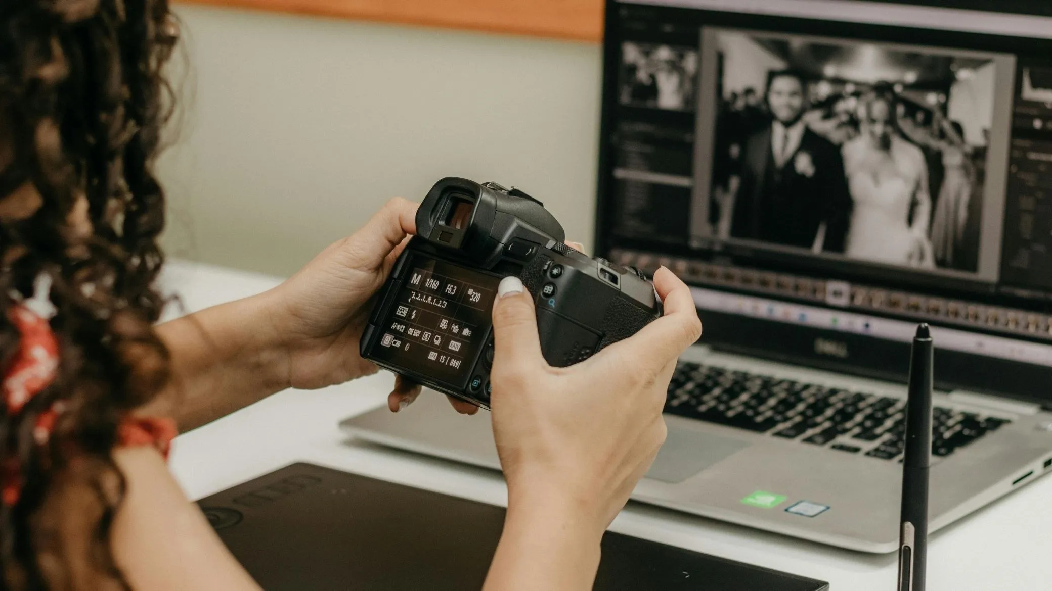 Des mains tiennent un reflex, avec un écran de retouche photo en arrière-plan